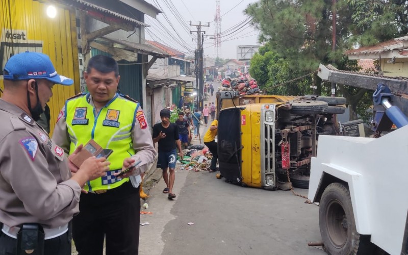 Tidak Kuat Menanjak Truk Sampah Terguling Menimpa Kios Jamu dan Dua Motor Ringsek